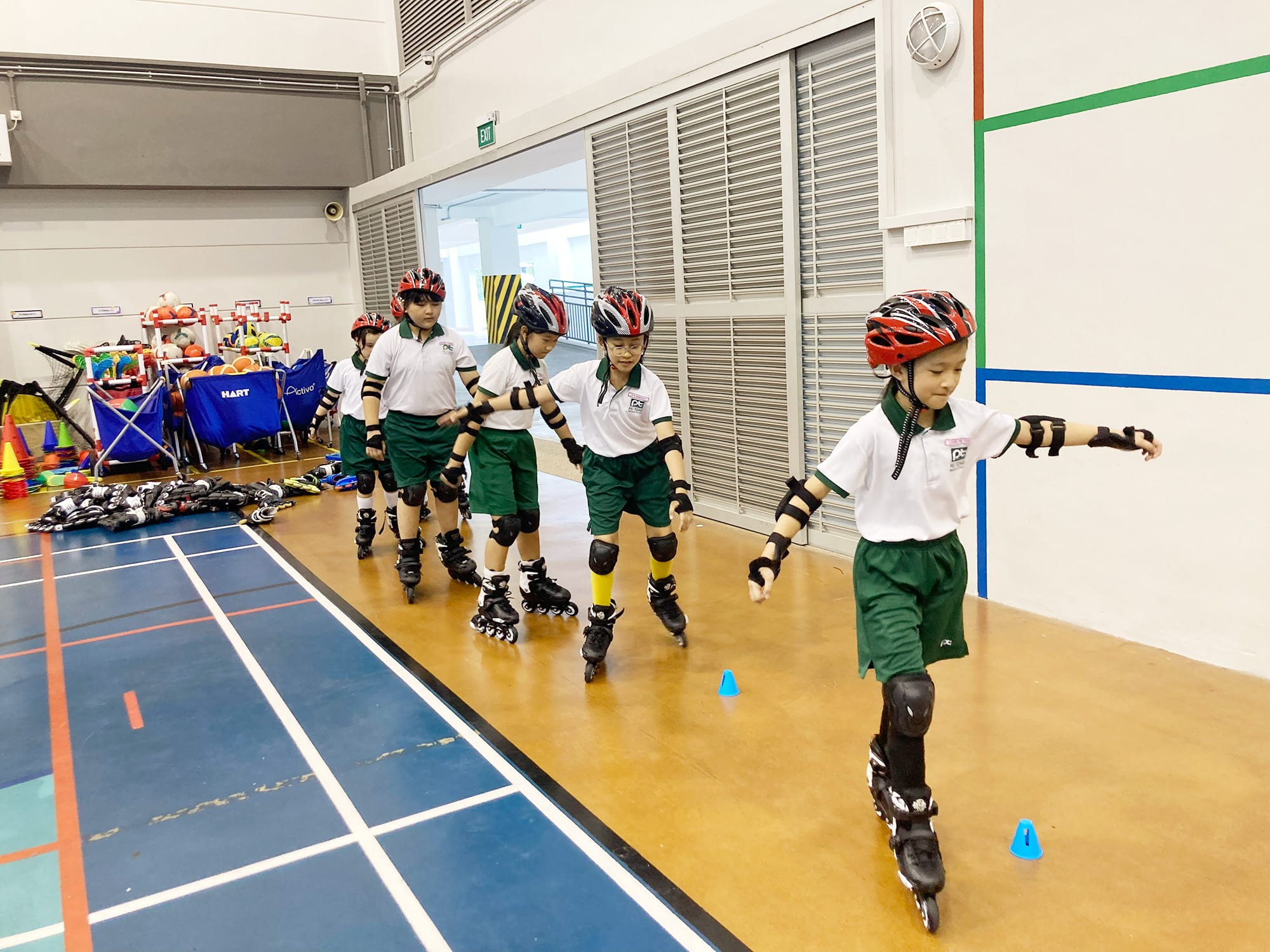 Students wearing helmets, wrist guards, elbow pads, knee pads, and inline skates carefully skate in a line through a cone course during an inline skating lesson.